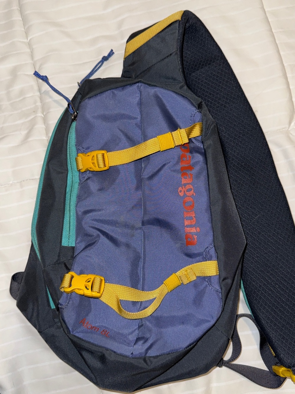 Patagonia navy sling pack with yellow straps and teal zipper